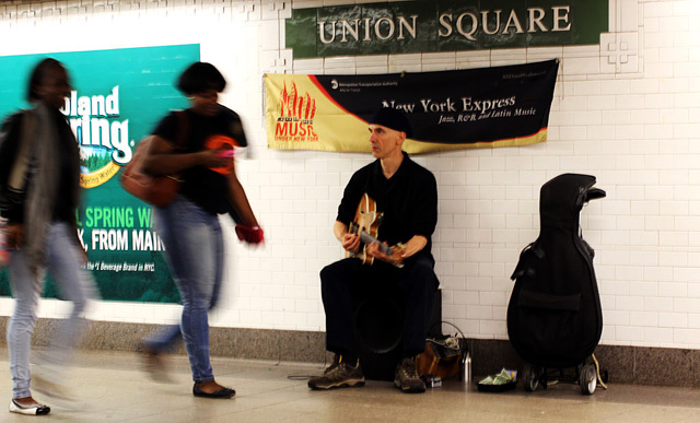A solo guitarist plays Latin Jazz music for travelers as they pass by.